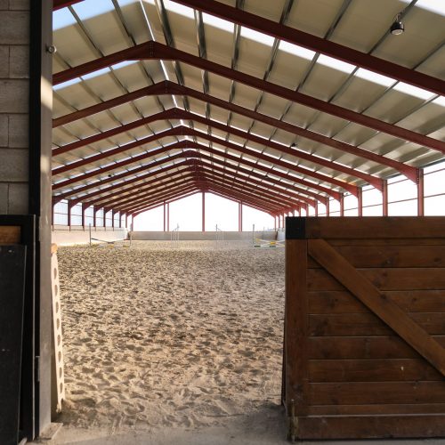Entry to an empty horse riding hall with jump fences.